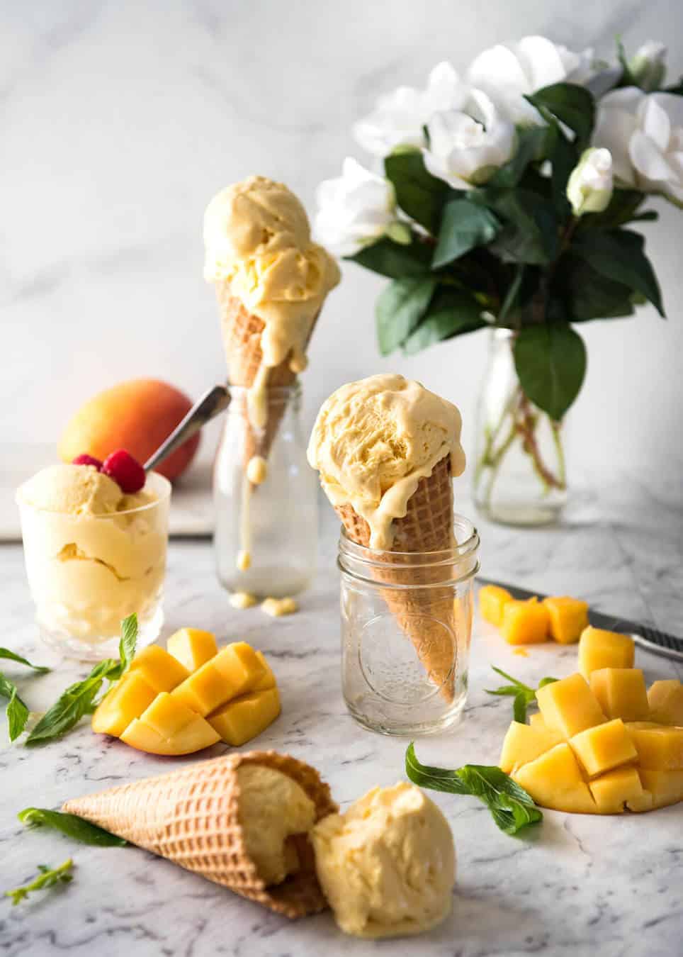 Homemade mango ice-cream in ice cream cones and in cups, with cheeks of cut mango on the side.